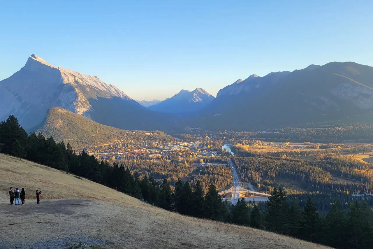 A breathtaking view of mountains surrounding a valley town, with a winding river and autumn foliage under a clear blue sky.